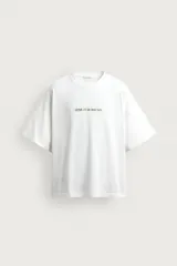 Camiseta blanca de corte relajado, con cuello redondo, manga corta y estampa frontal de texto pequeño en marrón.