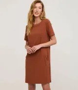 Vestido corto marrón oscuro, estilo camiseta, con escote redondo, mangas cortas y bolsillos laterales. El bajo es redondeado.