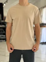 Remera clásica color beige, de manga corta, con cuello redondo y pequeño texto estampado en el pecho.