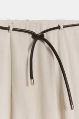 Falda larga de tiro medio, color beige claro, con caída amplia y cinturón fino negro anudado en la cintura.