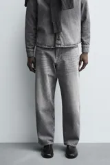Pantalón de jeans de algodón, color gris oscuro con efecto lavado. De tiro medio y corte relajado con pierna recta desde la cadera hasta el tobillo. Presenta cinco bolsillos y cierre frontal con botonadura.