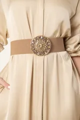 Cinto de malla elástica color beige con hebilla metálica circular bordada con piedras y strass.