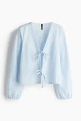 Blusa celeste a rayas blancas, de manga larga con elástico en los puños, escote en V y frente abierto con cierre de tiras para anudar.
