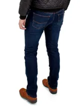 Pantalón de jean azul oscuro, corte ajustado, con bolsillos delanteros y traseros con costuras en color ocre.