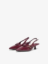 Zapatos slingback de cuero sintético acharolado color bordó, con punta fina, taco bajo y tiras cruzadas en el empeine con hebilla metálica dorada.