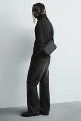 Bandolera negra con acabado engomado, compartimento principal con cierre de solapa y bolsillo con cremallera. Interior con bolsillo con cremallera. Asa de hombro ajustable.