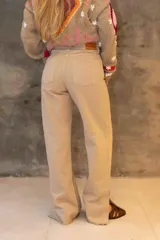 Pantalón vaquero de tiro alto y corte recto, con aberturas laterales en el bajo y detalles de cuero en la terminación. Presenta costuras decorativas en los bolsillos traseros y cierre con botón de guampa.