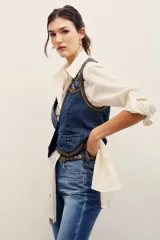 Chaleco de denim azul con bordados metalizados y pedrería en la parte superior delantera, escote en V y cierre frontal con botones metálicos.