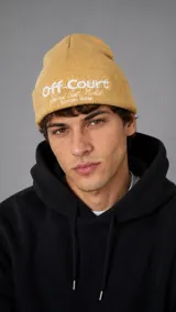 Gorro beanie de punto color mostaza con vuelta y texto bordado en blanco en el frente.