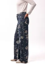 Jean de corte wide leg y tiro alto, confeccionado en denim azul oscuro con estampado floral en tonos suaves. Presenta diseño de cinco bolsillos y cierre frontal con botón.