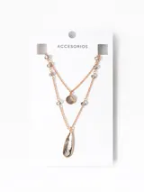 Collar doble dorado con cadena fina, dije circular con borde dorado y centro gris, y dije de cristal gris con borde dorado en forma de lágrima.