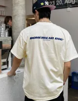Remera oversize color beige con estampado trasero en azul que dice "BOHEMIAN DSG" y "CERTIFIED AUTHENTIC STREETWEAR".