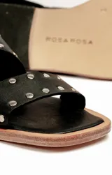 Sandalias bajas de cuero negro con tachas plateadas, tiras cruzadas y hebilla al tobillo.