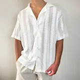 Camisa de tejido calado con textura, color blanco, de corte oversize, manga corta y cuello solapa con cierre frontal de botones.
