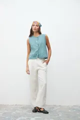 Pantalón de corte recto y tiro alto, confeccionado en lino color crudo. Presenta costuras verticales decorativas en el frente y cierre frontal con botón y cremallera.