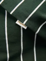 Remera de manga corta y cuello redondo con corte oversize, confeccionada en algodón. Presenta un diseño de rayas horizontales blancas sobre fondo verde oscuro.