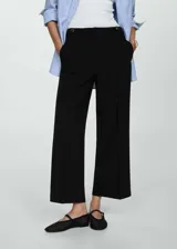 Pantalon de vestir negro de corte recto y diseño crop, confeccionado en tejido fluido con tiro medio. Presenta cierre frontal con botón, gancho y cremallera, además de detalles de botones decorativos en la cintura.