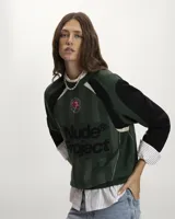 Suéter de punto Nude Project con diseño inspirado en camisetas de fútbol retro. Presenta un patrón de rayas verticales en tonos verde, negro y gris, con el logo de la marca en gran tamaño y una rosa bordada en el pecho. Posee cuello redondo acanalado y mangas largas con puños elásticos.