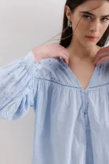 Camisa celeste de algodón con cuello en V, cierre frontal de botones y mangas largas abullonadas con detalles de bordado inglés.