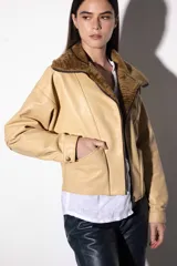 Chaqueta bomber color beige de cuero sintético con cuello de piel sintética marrón, cierre frontal con cremallera, bolsillos laterales y corte a la cintura.
