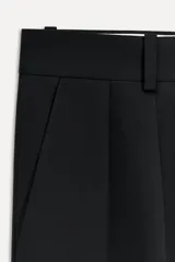 Pantalón negro de vestir con pinzas, tiro medio, trabillas en la cintura, bolsillos laterales y traseros con solapa. Cierre frontal con cremallera, botón y ganchos metálicos.