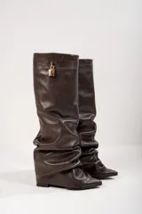 Botas de caña alta color negro, confeccionadas en cuero vegano. Presentan punta fina, caña arrugada y detalle de hebilla dorada en la parte superior.