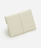 Billetera tipo sobre pequeña de color beige con textura croco en relieve y cierre con solapa y botón a presión.