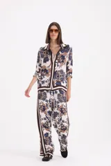 Pantalon de corte recto y holgado con estampado floral en tonos azules, marrones y crema. Presenta una franja lateral vertical en color marrón oscuro y cierre lateral.