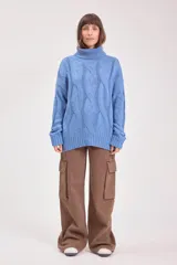 Sweater de punto color azul, con cuello alto y diseño de trenzas verticales. Presenta mangas largas con puños acanalados y un corte holgado.