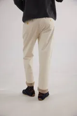 Pantalón recto de tiro medio confeccionado en pana con lycra. Presenta pinzas frontales, bolsillos laterales y traseros, y cierre con botón dorado. El diseño destaca por el detalle de paño espigado en el interior del ruedo, visible al doblarlo, y un pin bordado decorativo en el bolsillo delantero.
