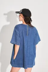 Vestido corto de denim azul con corte holgado, mangas cortas y bolsillo frontal con logo bordado. Cuenta con cierre metálico en la espalda.
