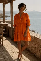 Vestido corto de lino color naranja, con cuello mao, escote en V con botones frontales, mangas largas con presillas para arremangar y diseño de cortes escalonados con vuelo.