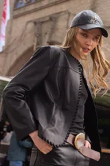 Campera de cuero negro con detalles de costuras decorativas en los bordes delanteros y mangas largas.