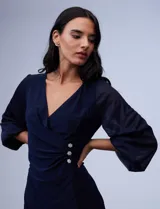 Vestido azul de RM Richards en seda fría, con escote en V cruzado, cintura drapeada, mangas largas de gasa y aplique de botones en el lateral.