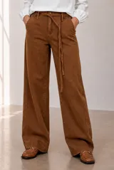 Jean de corte wide leg en color marrón, tiro medio con trabillas para cinturón y un cordón fino integrado como lazo. Cuenta con bolsillos laterales y traseros tradicionales.
