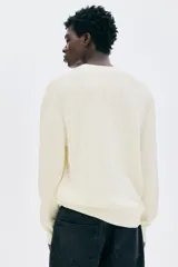 Buzo de algodón fino color crema, con cuello redondo y manga larga. Presenta un tejido de punto acanalado vertical y un bajo recto.