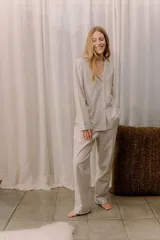 Pijama de viyela de algodón en tono beige con sutil estampado a rayas. La camisa presenta cuello solapa, cierre frontal con botones y detalles de tela estampada con flores en los puños y bolsillo. El pantalón es de corte recto con elástico en la cintura y detalles florales en los bajos.