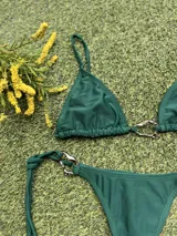 Conjunto de bikini verde con corpiño triangular con argolla metálica en el centro y bombacha colaless con tiras para atar y argollas en los costados.