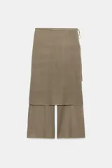 Pantalón de punto fino color beige, de corte recto y holgado, con cintura elástica y una falda pareo superpuesta con nudo lateral.