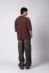 Remera de tejido de punto con textura calada, color crema con rayas verticales sutiles. Presenta cuello en V, mangas cortas con franjas laterales en color marrón oscuro y logo bordado en el centro del pecho.