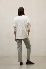 Buzo de cuello redondo color blanco marfil, con hombros caídos y diseño oversize. Cuenta con puños, cuello y bajo acanalados, además de detalles de costura decorativa en la parte frontal del cuello.