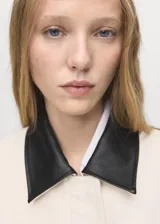 Chaqueta recta de algodón estilo vaquero, color blanco, con manga larga, cuello camisero de efecto piel en contraste, cierre oculto de cremallera y botones, y dos bolsillos delanteros de parche con solapa.