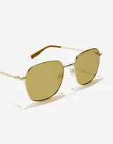 Lentes de sol con marco metálico dorado de forma geométrica y cristales en tono amarillento. Presentan patillas finas con terminales en color marrón.