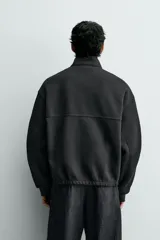 Cazadora de corte boxy fit en tejido acanalado con interior polar. Presenta cuello subido, manga larga con puños, bolsillos frontales tipo canguro y cierre frontal de cremallera oculta por solapa con botones a presión.