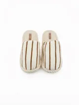 Pantuflas abiertas de estilo mule, con capellada de peluche color crema con rayas negras horizontales y plantilla de pana acanalada en tono beige.
