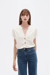 Blusa de viscosa color blanco, de corte holgado, con cuello en V y cierre frontal parcial de botones grandes con efecto carey.