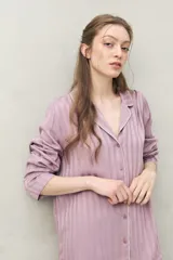 Camisa de pijama color blanco tiza con rayas verticales en relieve, de silueta clásica y caída fluida. Presenta cuello camisero, cierre frontal con botones y detalles de vivo rosado en cuello, puños y solapas.