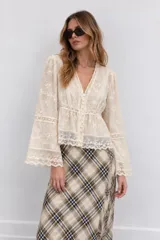 Blusa marfil con detalles de encaje y bordados florales transparentes, con escote en V, cierre frontal abotonado y mangas largas acampanadas.