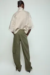 Camisa de corte holgado confeccionada en mezcla de lyocell, con estampado de rayas verticales en tonos neutros y azules. Presenta cuello redondo con lazada frontal, cierre con botones ocultos y mangas amplias por debajo del codo.