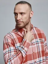 Camisa de manga larga confeccionada en franela de algodón, con diseño de cuadros en tonos rojos, rosados y detalles en azul. Presenta cuello con botones, cierre frontal abotonado y un bolsillo en el pecho con detalle metálico.